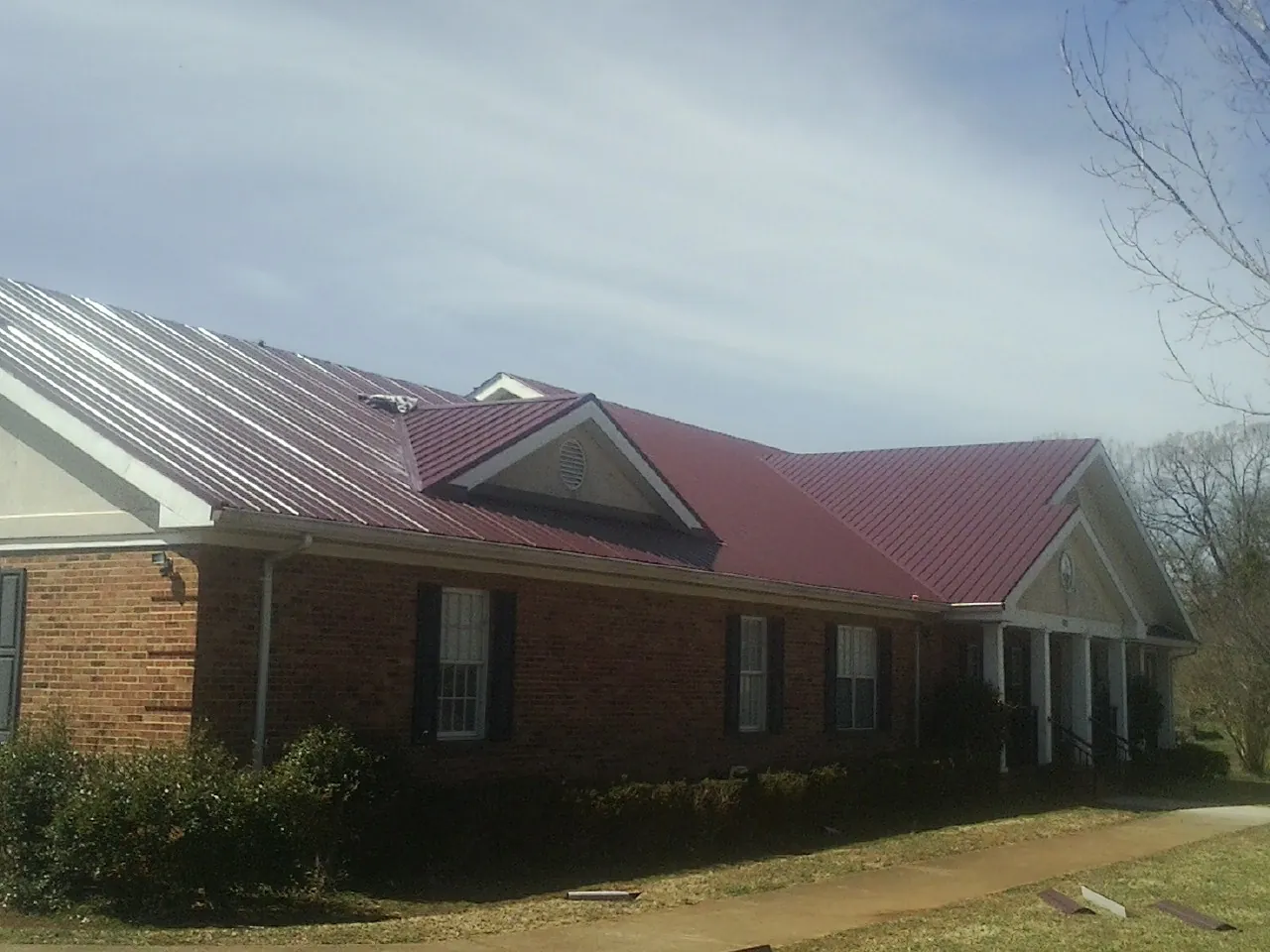 Red metal roof with gabled entries on a long brick building, from a Hail Damage Roof Repair job in Candia