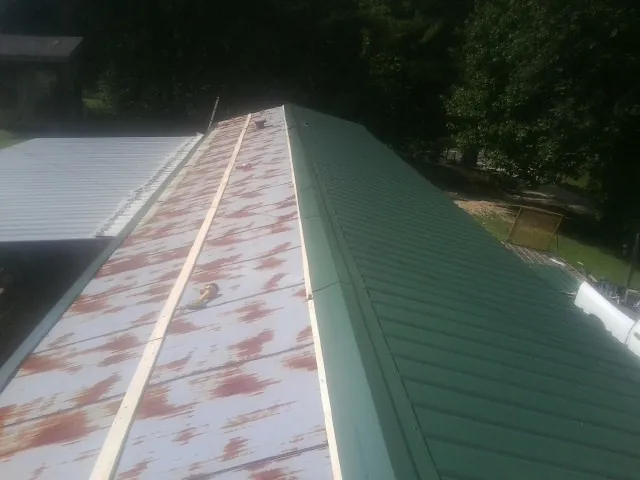 Old rusted panels beside newly installed green metal roofing — Wind Damage Roof Repair by Roofing Brothers in Candia
