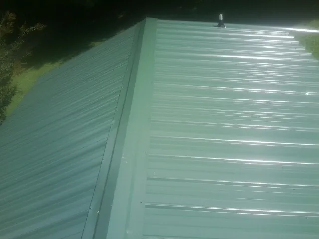 New green metal panels meeting at the ridge of a roof — Flat Roof Repair work by our crew in Candia