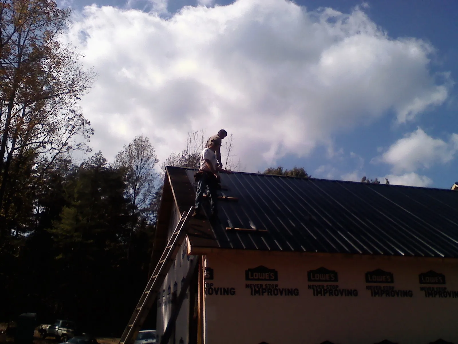 Roofer fastening dark metal panels high against a cloudy sky, from a Roof Inspection job in Candia
