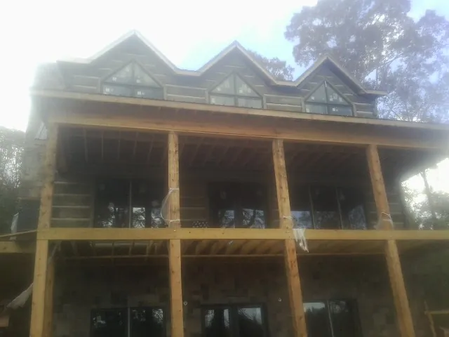 Dormers and porch framing on a large log home under construction — Roof Coating work by our crew in Candia