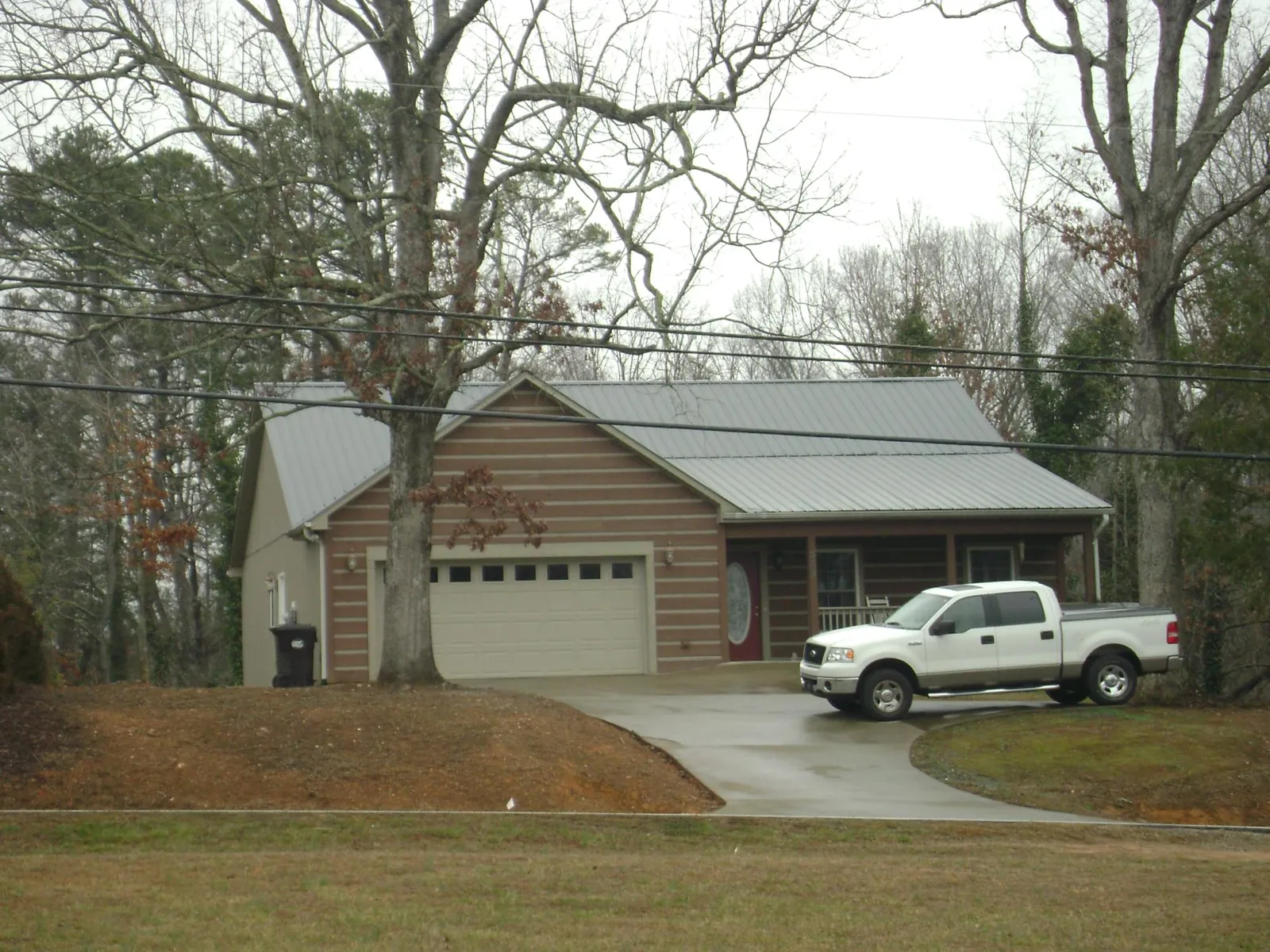 Gray metal roof on a log sided house with an attached two car garage in Candia