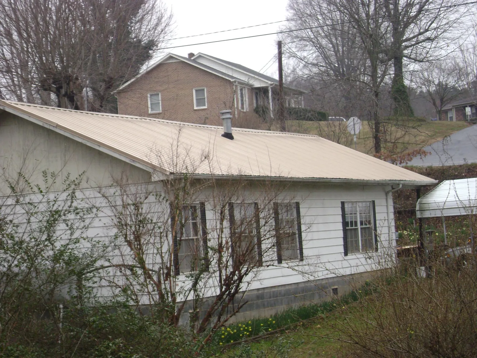 Tan metal roof on a white sided house set into a hillside — Commercial Roofing by Roofing Brothers in Candia