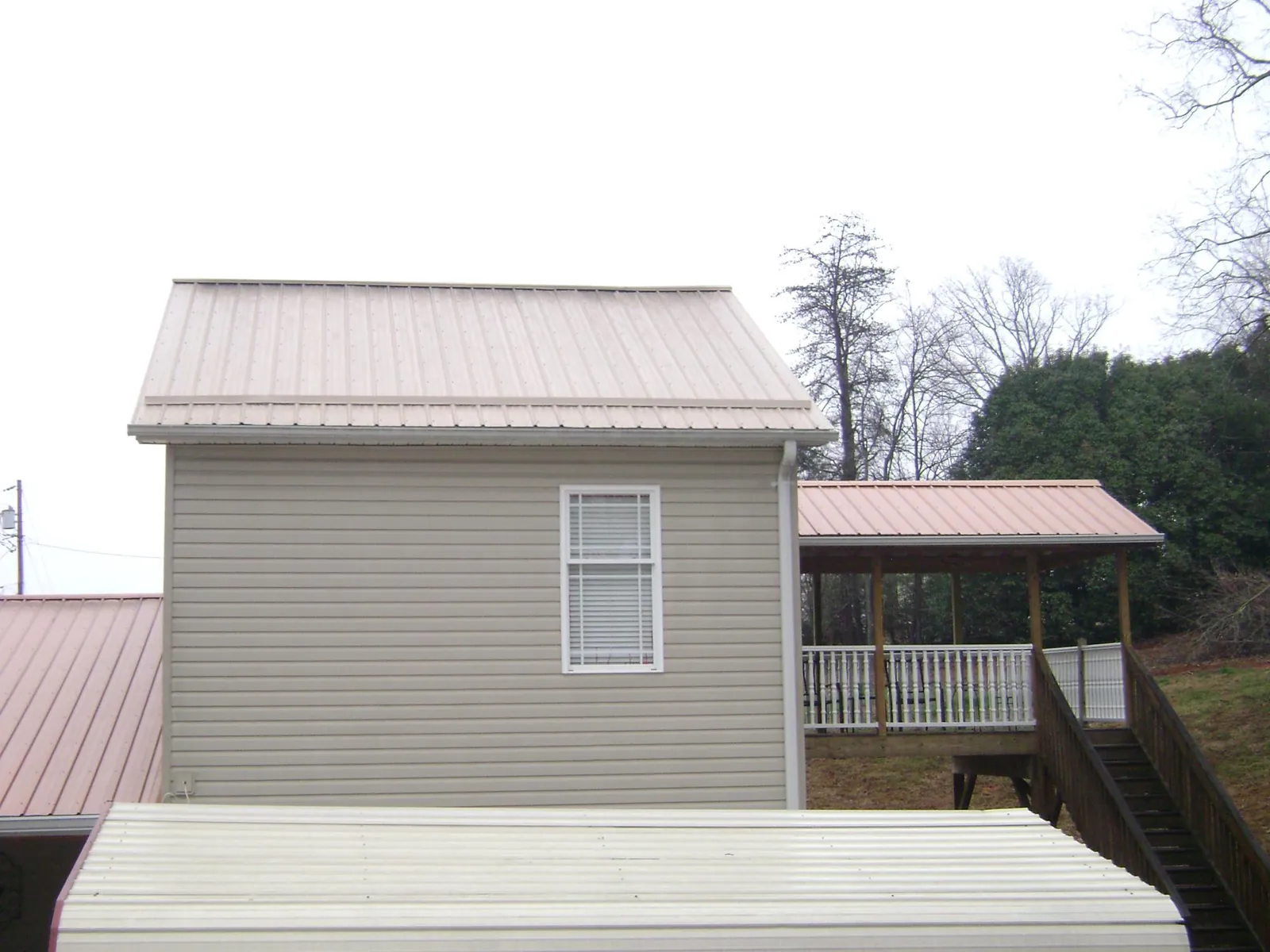 Tan metal roofs on a two story addition and attached porch, from a Roof Replacement job in Candia
